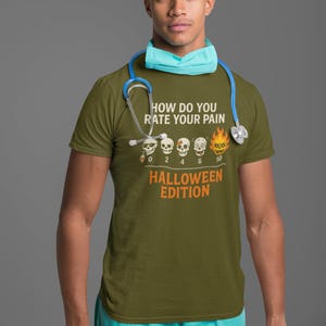 May include: Olive green t-shirt with the text "HOW DO YOU RATE YOUR PAIN" and "HALLOWEEN EDITION" in orange. The shirt features a pain scale with skulls, ranging from 0 to 10. A person is wearing the shirt, a blue surgical cap, and a stethoscope.