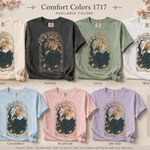 May include: Seven short-sleeved crew neck t-shirts in ivory, pepper, sage, white, chambray, blossom, and orchid. Each shirt features a graphic print of a fox with multiple tails under a full moon within an ornate, arched, gold-toned frame.