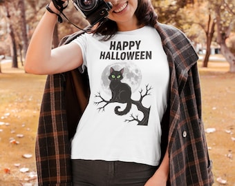 May include: White t-shirt with the text "HAPPY HALLOWEEN" above a black cat perched on a tree branch in front of a full moon. The cat has green eyes. The shirt is worn by a person.