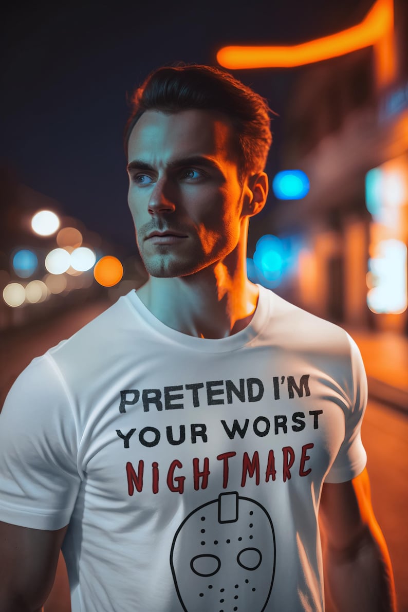 May include: White t-shirt with the text "PRETEND I'M YOUR WORST NIGHTMARE" in black and red, and a hockey mask graphic. The shirt is worn by a person in an outdoor setting with blurred lights in the background.