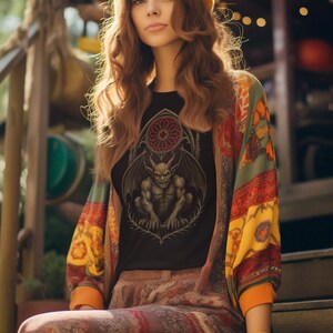 May include: A person wearing a black t-shirt with a gargoyle graphic, a colorful patterned jacket, and a yellow beret. The outfit has a bohemian style. The person is sitting on wooden steps.