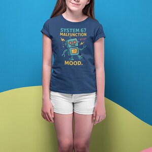May include: Navy blue t-shirt with a robot graphic and the text "SYSTEM 67 MALFUNCTION MOOD." The robot is light blue with yellow accents. The person is wearing white shorts and a purple headband.