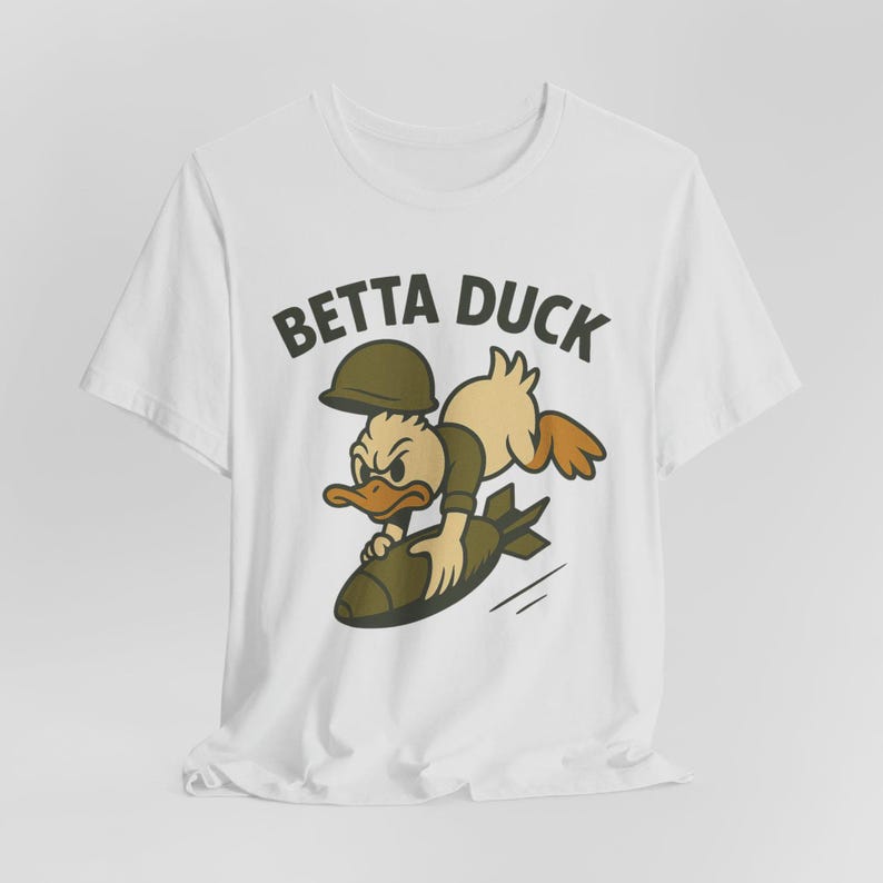 May include: White t-shirt featuring a cartoon duck wearing a military helmet and uniform, riding a bomb. The text "BETTA DUCK" is printed above the duck. The duck has an angry expression.