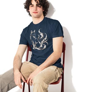 May include: A navy blue short-sleeved t-shirt featuring a white, brushstroke-style graphic of a multi-tailed fox sitting in profile. The design includes a small red square stamp detail near the base of the fox illustration on the chest.