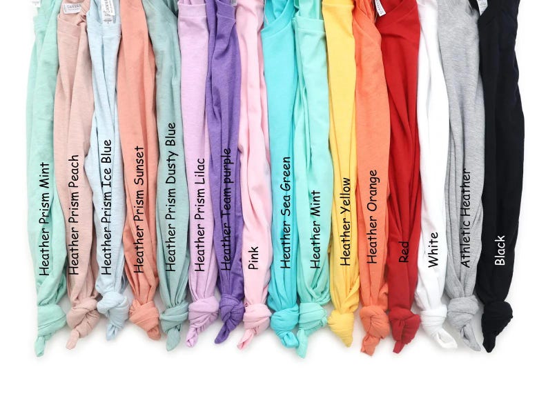 May include: A selection of t-shirts in a range of colours: mint, peach, ice blue, sunset, dusty blue, lilac, team purple, pink, sea green, yellow, orange, red, white, athletic heather, and black. Each is labelled with its colour.