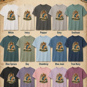 May include: A collection of fifteen short-sleeve t-shirts in various colors, each featuring a graphic of an angel with the text 'HEAVENLY BODY'. The colors include white, ivory, pepper, grey, seafoam, blue spruce, bay, chambray, blue jean, true navy, black, violet, blossom, orchid, and berry.