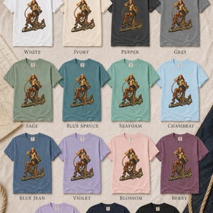 May include: A collection of Comfort Colors 1717 t-shirts in fourteen colors, each featuring a graphic of a person sitting on an anchor with the text Anchors Aweigh. Colors include white, ivory, pepper, grey, sage, blue spruce, seafoam, chambray, blue jean, violet, blossom, berry, orchid, true navy, and black.