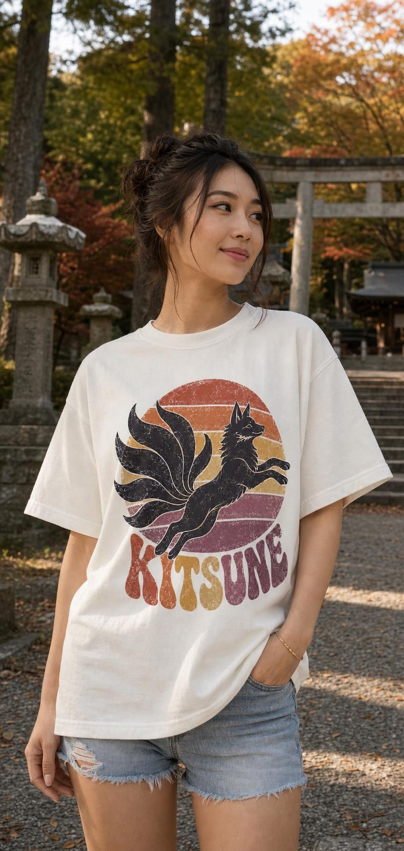 May include: An off-white short-sleeve t-shirt featuring a graphic of a black nine-tailed fox leaping in front of a circular sunset design with horizontal stripes in orange, red, and purple, with the word KITSUNE printed in a bold, retro font.