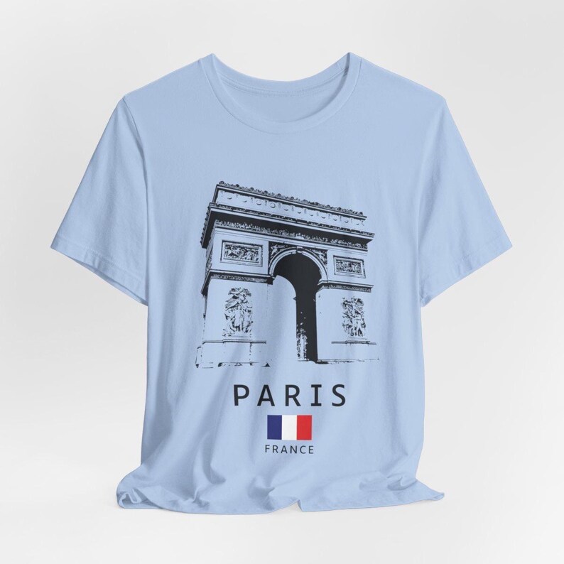 Puede incluir: Camiseta azul claro con una ilustraci&oacute;n en blanco y negro del Arco del Triunfo de Par&iacute;s. Debajo de la imagen, se lee la palabra "PARIS", junto con la bandera francesa y la palabra "FRANCE".