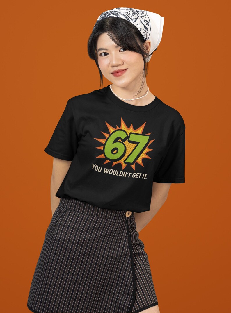 May include: Black t-shirt with the number "67" in green, set against a yellow burst design. The text "YOU WOULDN'T GET IT" is below the number. The person is wearing a white bandana and a striped skirt.