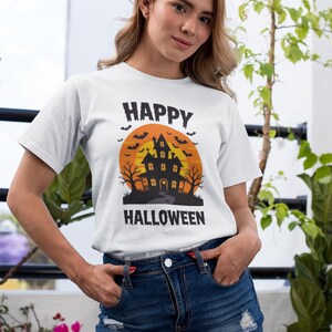 May include: White t-shirt with a Halloween design. The graphic features a haunted house silhouette against an orange sunset, with bats and the words "HAPPY HALLOWEEN". The shirt is paired with a denim skirt.