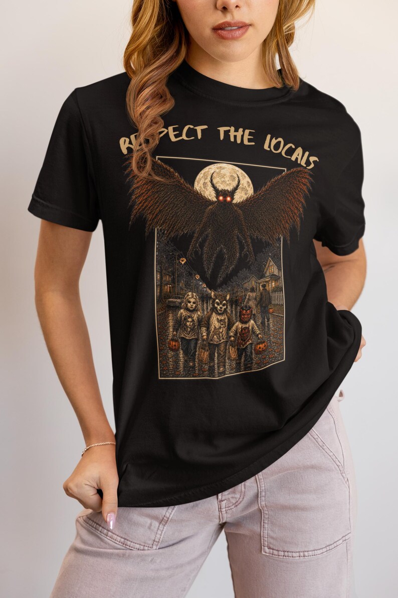 May include: A black short-sleeved t-shirt featuring a graphic print with the text "RESPECT THE LOCALS" in a tan font. The illustration depicts a large winged creature hovering above three children in costumes on a street under a full moon.