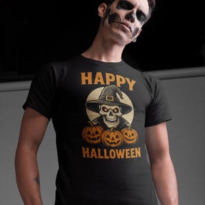 May include: Black t-shirt with a Halloween-themed graphic. The design features a skull wearing a witch hat, surrounded by three carved pumpkins. The words "HAPPY HALLOWEEN" are printed above and below the central image in orange.