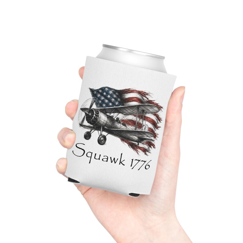 May include: A white foam can cooler featuring a black and white sketch of a biplane flying in front of a distressed American flag. The text Squawk 1776 is printed in a black serif font below the illustration of the vintage aircraft.