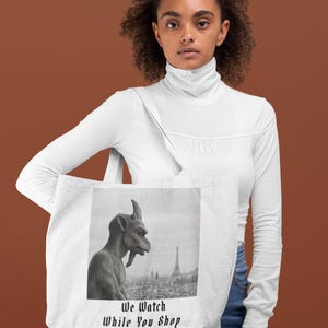 Op de afbeelding: Witte draagtas met een zwart-wit afbeelding van een waterspuwer en de Eiffeltoren. De tekst "We Watch While You Shop" staat onder de afbeelding.