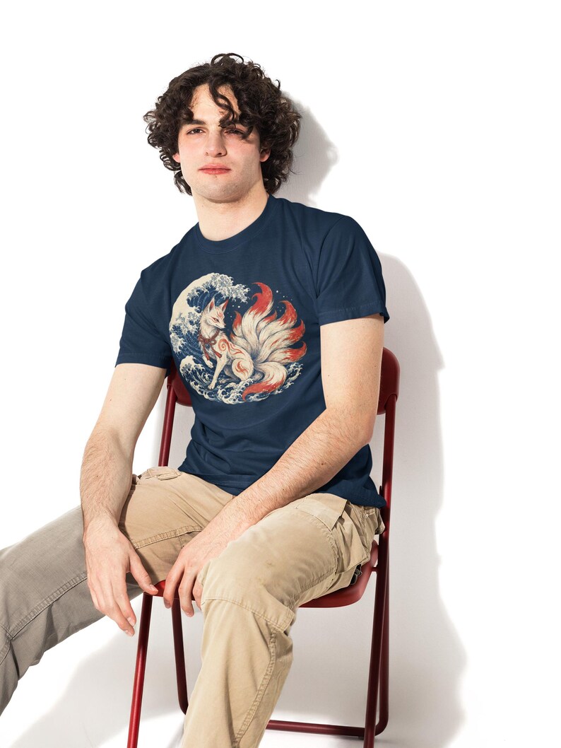 May include: A navy blue short-sleeved t-shirt featuring a circular graphic print of a white nine-tailed fox with red markings standing amidst stylized blue and white ocean waves, paired with light tan cargo pants and gray trousers.