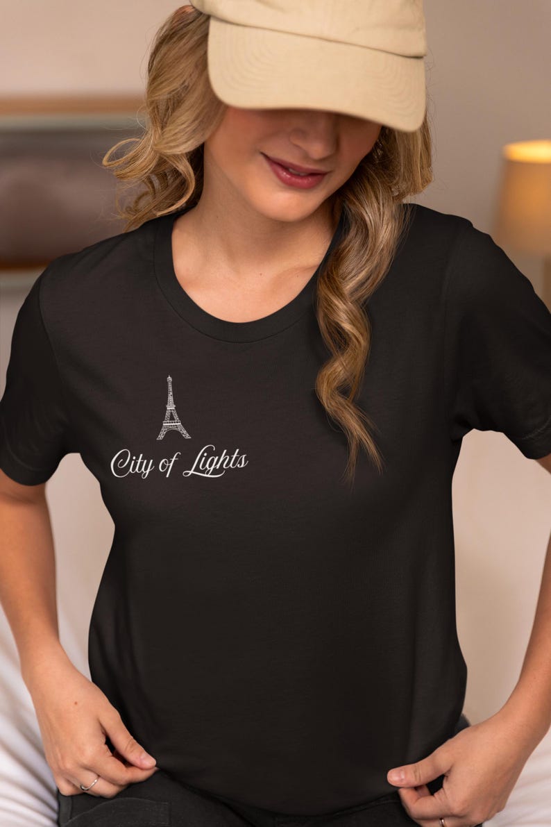 May include: Black t-shirt featuring a white Eiffel Tower design and the text "City of Lights." The shirt has a classic crew neck and short sleeves. The design is located on the upper left chest area.