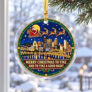 May include: A round clear acrylic Christmas ornament featuring a stained glass style illustration of the Pittsburgh skyline at night with Santa and his reindeer flying above. The text reads MERRY CHRISTMAS TO YINZ AND TO YINZ A GOOD NIGHT.