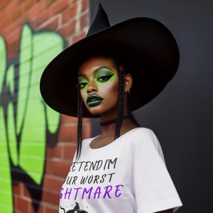 May include: A person wearing a black witch hat and a white t-shirt with the text "PRETEND I'M YOUR WORST NIGHTMARE" in black and purple. The person has green eye makeup and dark green lipstick. The background includes a brick wall with green graffiti.
