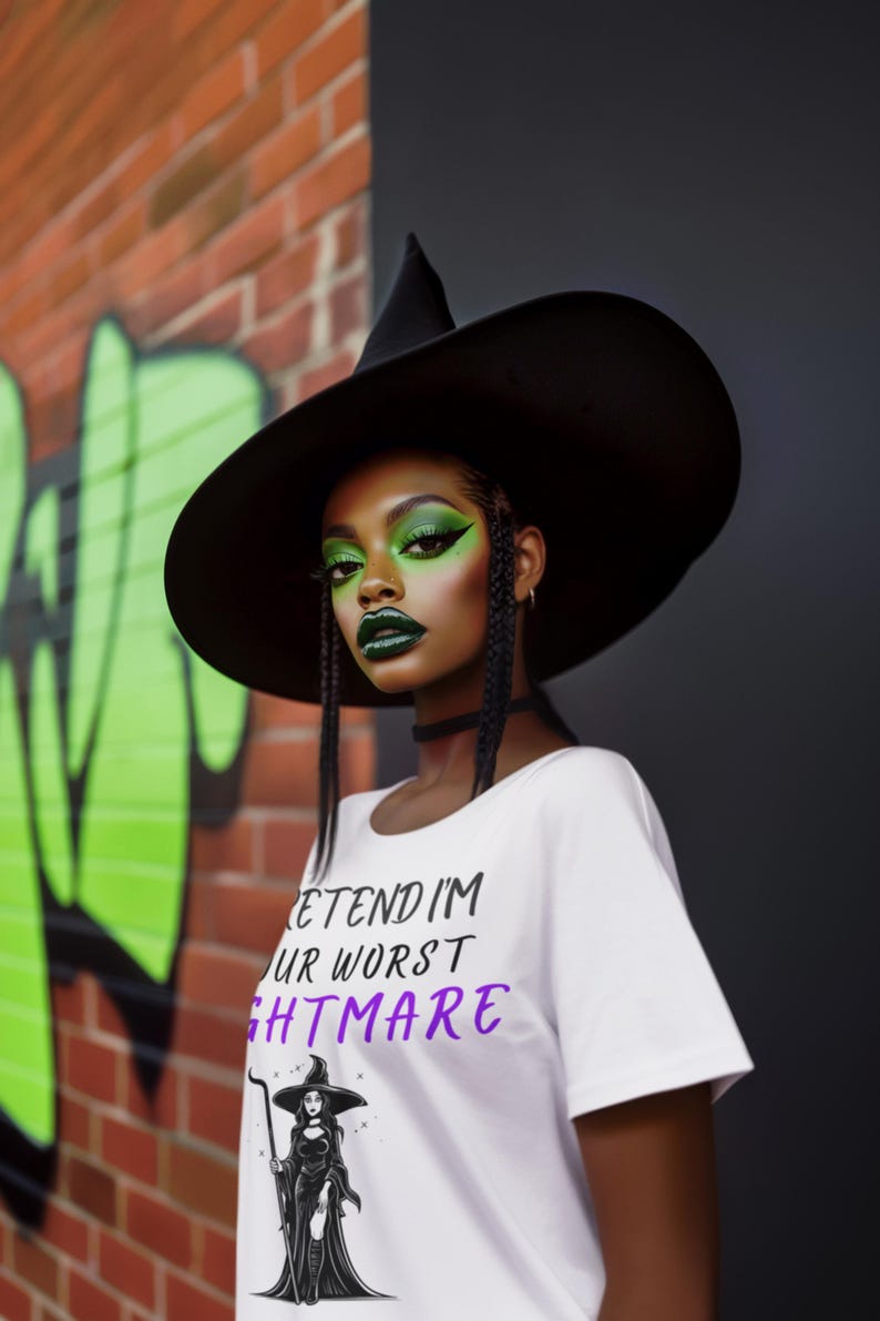 May include: A person wearing a black witch hat and a white t-shirt with the text "PRETEND I'M YOUR WORST NIGHTMARE" in black and purple. The person has green eye makeup and dark green lipstick. The background includes a brick wall with green graffiti.