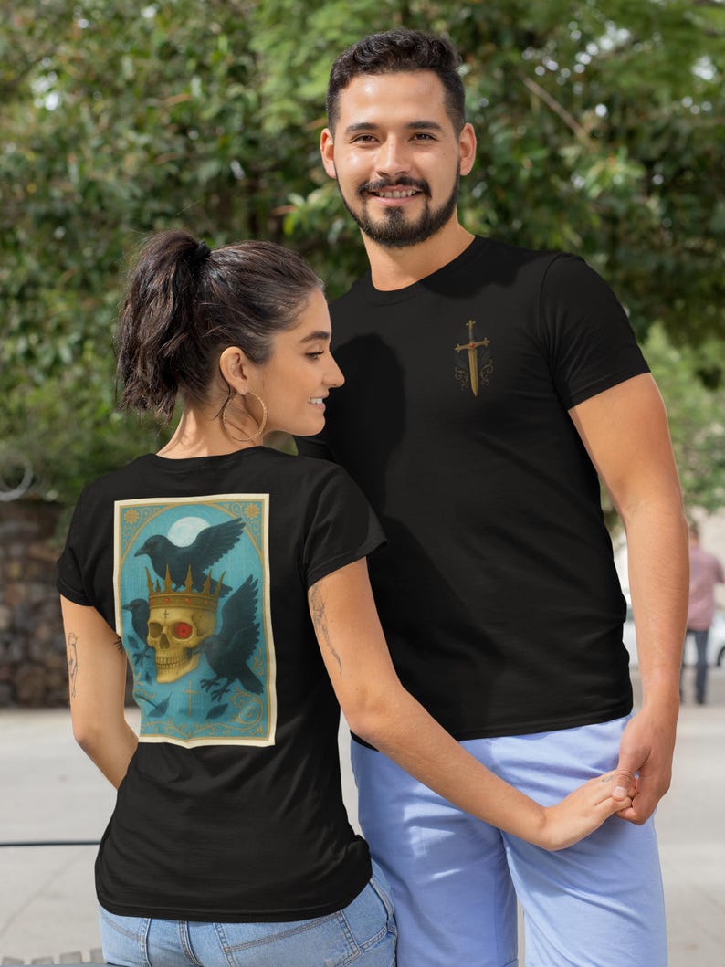 May include: Black t-shirts with graphic designs. One shirt has a gold sword design, the other a skull wearing a crown, with ravens and a moon. The shirts are worn by a couple.