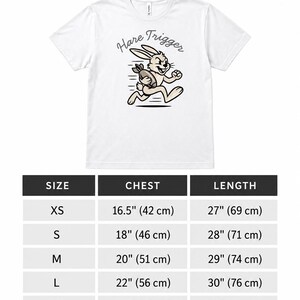Puede incluir: Una camiseta blanca de manga corta con un gr&aacute;fico de un conejo corriendo que sostiene una granada con el texto Hare Trigger. Debajo de la camiseta hay una tabla de tallas que enumera las medidas de pecho y largo en cent&iacute;metros de 42 a 71 cm.