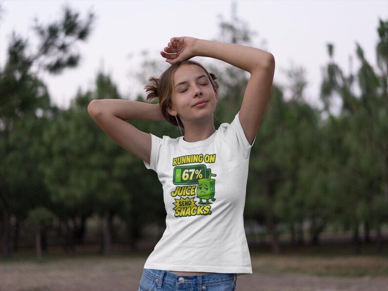 Pu&ograve; includere: T-shirt bianca con grafica umoristica. Il design presenta un personaggio di cartone del succo verde con la scritta "Running on 67% Juice, Send Snacks". La maglietta &egrave; indossata da una persona con le braccia alzate.