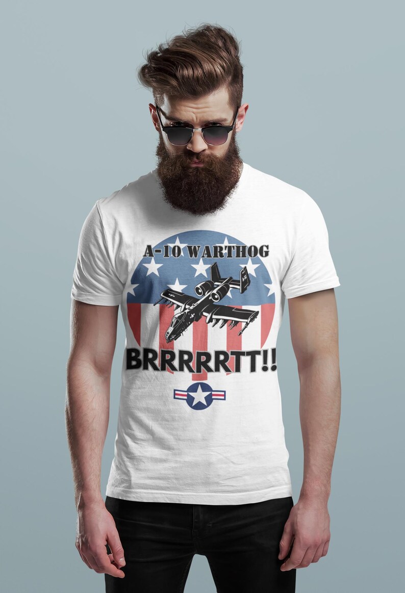 Puede incluir: Camiseta blanca con un gr&aacute;fico del A-10 Warthog. El dise&ntilde;o incluye el texto "A-10 WARTHOG" y "BRRRRRTT!!" encima y debajo del avi&oacute;n, sobre un c&iacute;rculo rojo, blanco y azul con estrellas y rayas, y un emblema de la Fuerza A&eacute;rea de EE. UU.