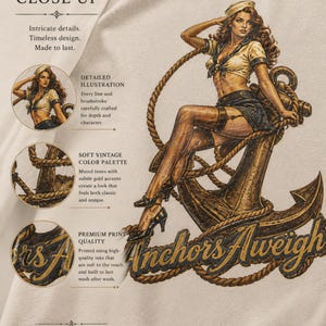 May include: A beige t-shirt featuring a detailed illustration of a person in a sailor-style outfit sitting on a large anchor. The graphic includes the text Anchors Aweigh in a dark script font, surrounded by rope details and descriptive text labels.