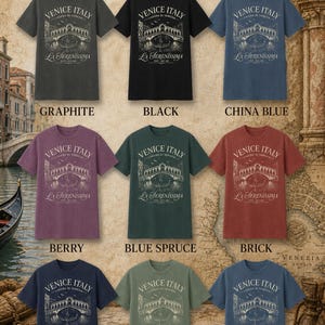 May include: A collection of nine short-sleeved t-shirts in graphite, black, china blue, berry, blue spruce, brick, true navy, sage, and denim. Each shirt features a white graphic print of a bridge, a gondola, and the text Venice Italy.