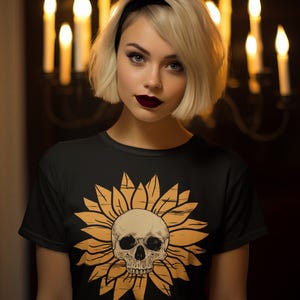 May include: Black t-shirt featuring a skull within a sunflower design, with the text "Happy Halloween" below. The image is set against a dark background with lit candles, creating a spooky, festive atmosphere.