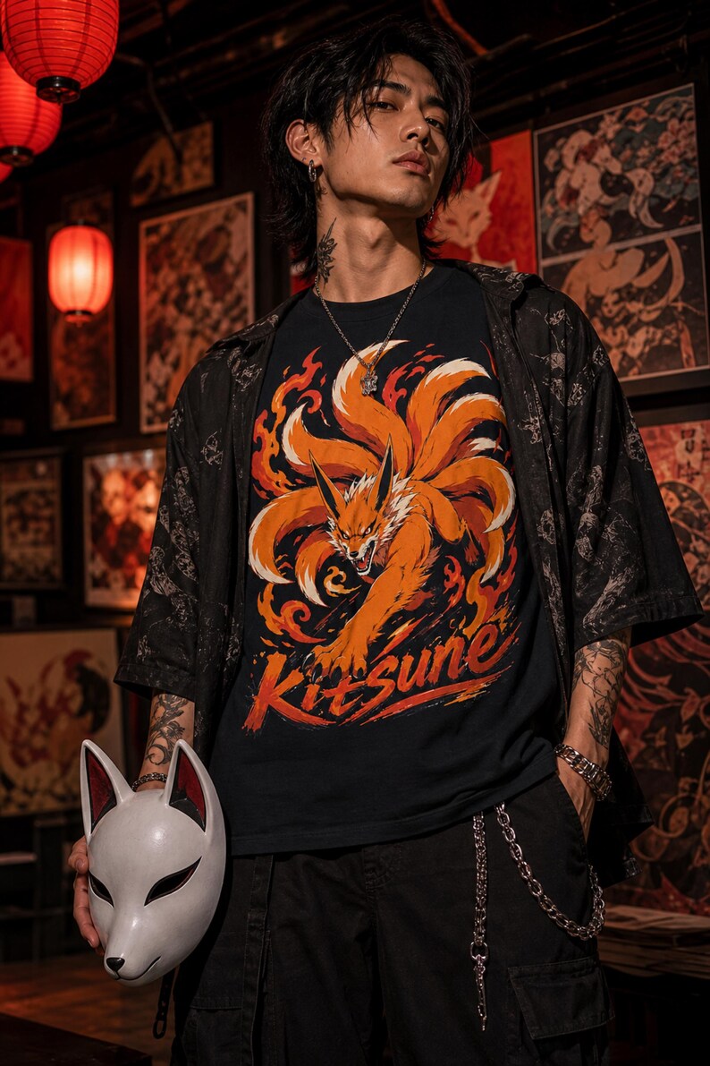 K&ouml;nnte beinhalten: Ein schwarzes T-Shirt mit einer Grafik eines orangefarbenen neunschw&auml;nzigen Fuchses, umgeben von Flammen, mit dem darunter gedruckten Text Kitsune. Das T-Shirt wird unter einem schwarzen kurz&auml;rmeligen Hemd getragen und eine wei&szlig;e Fuchsmaske.
