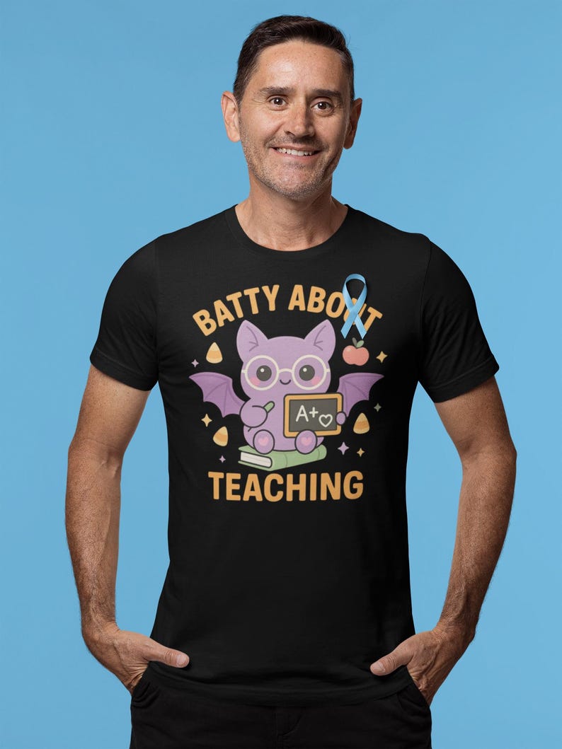 K&ouml;nnte beinhalten: Schwarzes T-Shirt mit einer Cartoon-Fledermaus mit Brille, die eine Tafel mit einem A+ h&auml;lt. Der Text "BATTY ABOUT TEACHING" ist in Gold gehalten, mit einem blauen Band und einer Apfelgrafik. Ein lustiges Design f&uuml;r Lehrer.