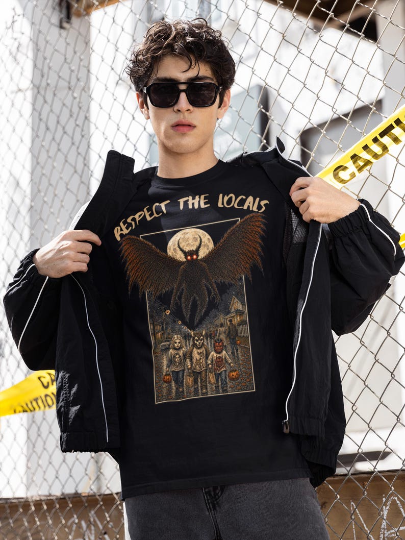 May include: A black t-shirt featuring a graphic print with the text "RESPECT THE LOCALS" above a winged creature with glowing red eyes and a full moon. Below, three figures in costumes stand on a street at night, each holding a pumpkin bucket.