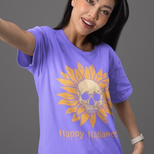 May include: A purple t-shirt featuring a yellow sunflower design with a skull in the center. The words "Happy Halloween" are printed in orange below the graphic. The shirt is a short-sleeved crew neck.
