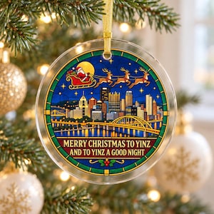 May include: A round, clear acrylic Christmas ornament featuring a stained-glass style illustration of the Pittsburgh skyline at night, with Santa and his reindeer flying above. The text reads, "MERRY CHRISTMAS TO YINZ AND TO YINZ A GOOD NIGHT."