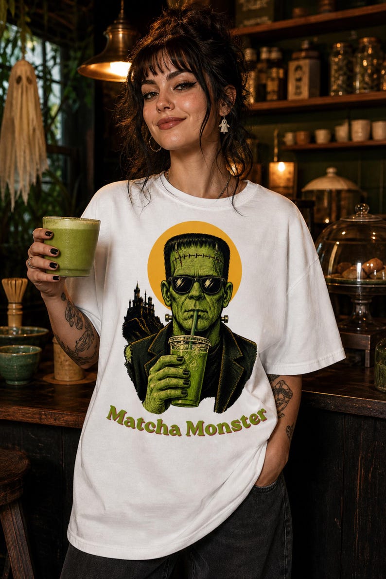 Może przedstawiać: Biały t-shirt z grafiką zielonego potwora w okularach przeciwsłonecznych, pijącego z przezroczystego kubka przez słomkę. Za potworem znajduje się ż&oacute;łte koło i sylwetka ciemnego zamku. Poniżej znajduje się napis Matcha Monster.