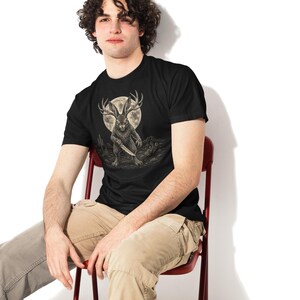 K&ouml;nnte beinhalten: Ein schwarzes T-Shirt mit kurzen &Auml;rmeln und einer grafischen Illustration eines Jackalopen, der ein Messer h&auml;lt. Das Wesen steht in einer W&uuml;stenlandschaft unter einem gro&szlig;en Vollmond. Das Design ist in Grau-, Wei&szlig;- und Schwarzt&ouml;nen gehalten.