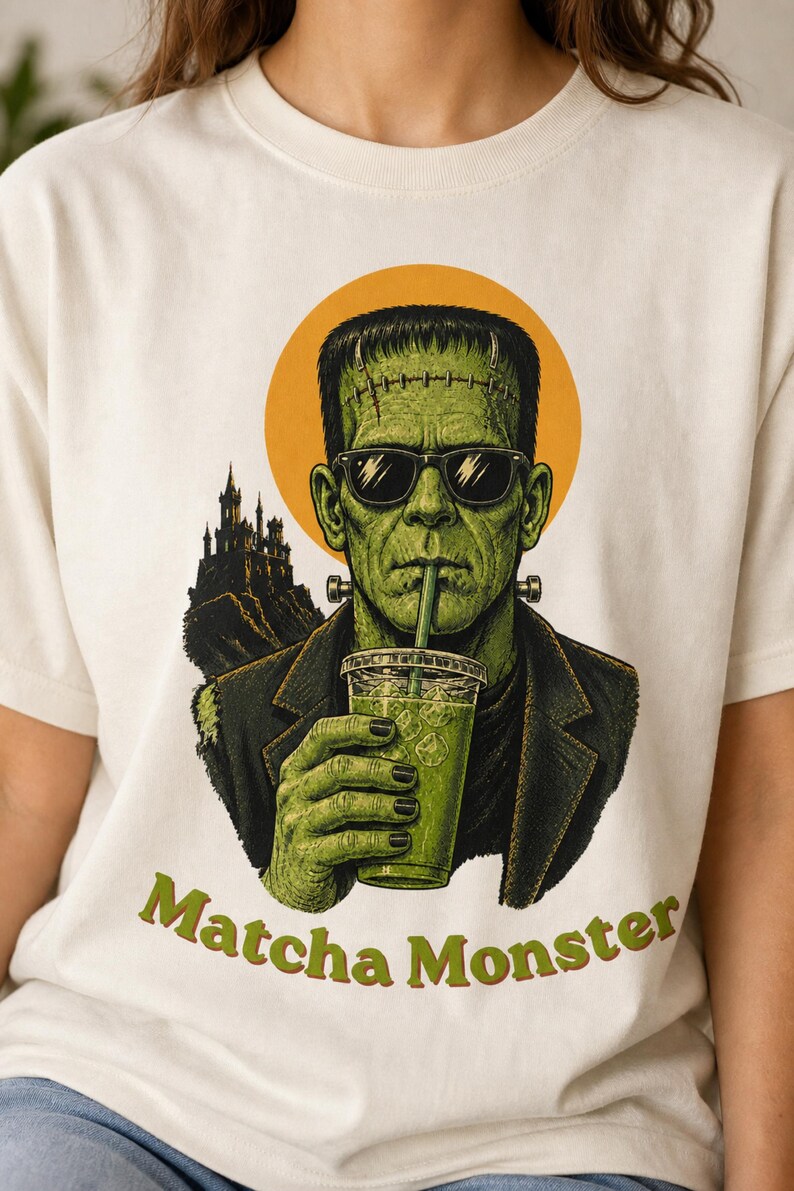Może przedstawiać: Kremowy t-shirt z grafiką przedstawiającą zielonego potwora w okularach przeciwsłonecznych i ciemnej marynarce, pijącego zielony nap&oacute;j z przezroczystego kubka ze słomką. Za postacią widoczny jest zarys zamku oraz ż&oacute;łte koło z napisem Matcha Monster.