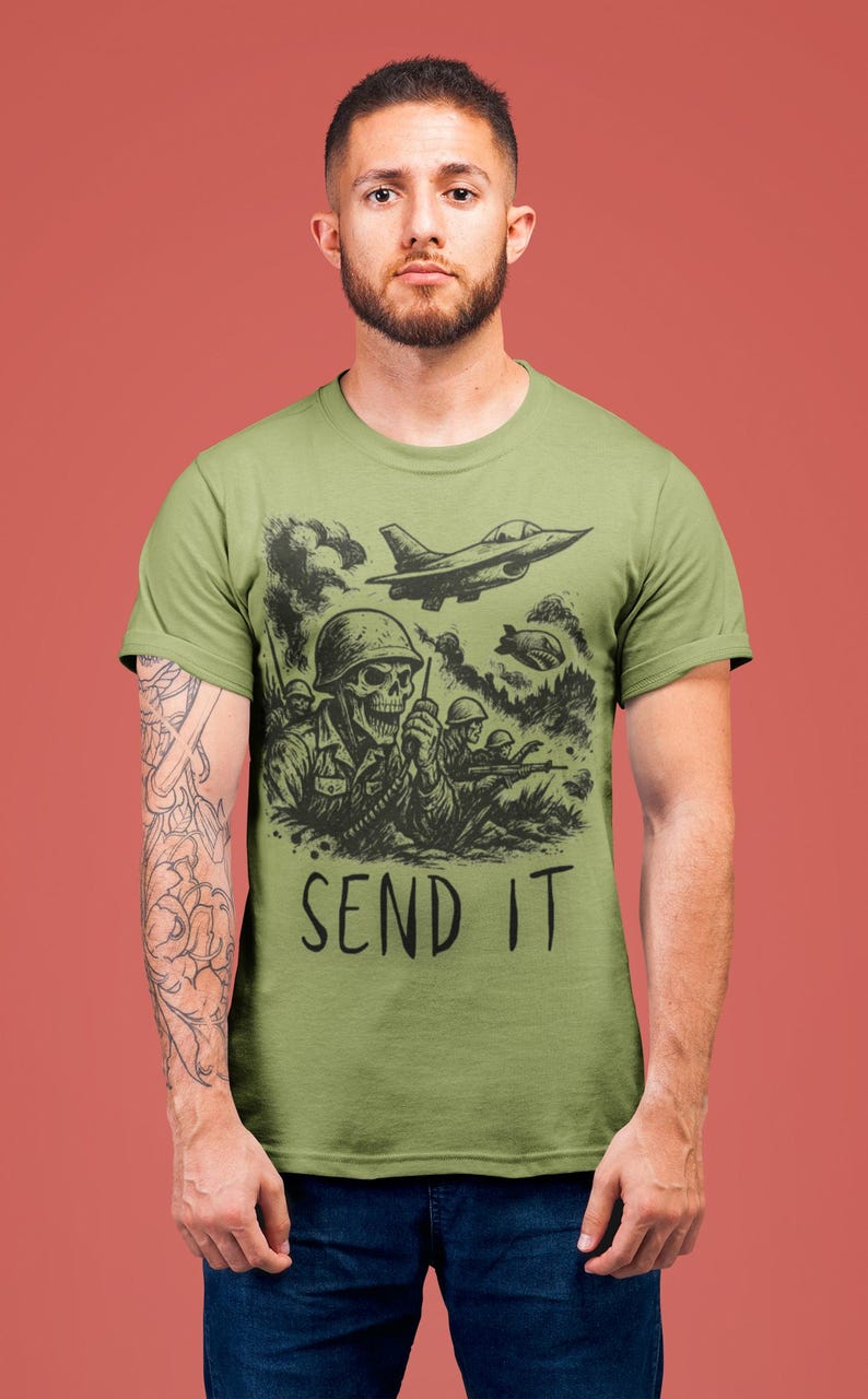 Puede incluir: Camiseta verde oliva con una ilustraci&oacute;n en blanco y negro de un soldado esqueleto con una radio, rodeado de otros soldados y aviones de combate. El texto "SEND IT" est&aacute; impreso debajo del gr&aacute;fico.