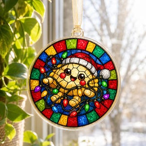 May include: A circular stained glass ornament featuring a yellow turtle wearing a red and white Santa hat, tangled in colorful Christmas lights. The border consists of alternating red, blue, green, and yellow glass segments, suspended by a gold ribbon.