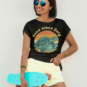 May include: Black t-shirt with a turtle graphic and the text "Good Vibes Only." The turtle is teal and the sunset is orange and yellow. The person is wearing yellow shorts and holding a turquoise skateboard.