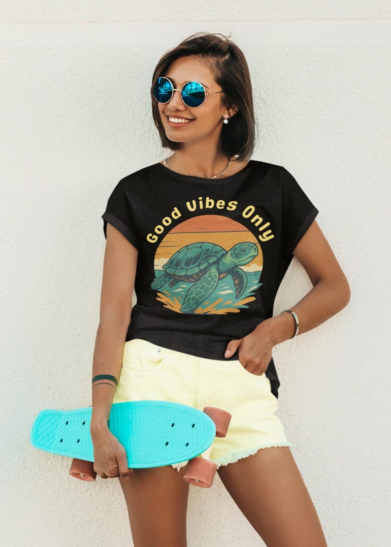 May include: Black t-shirt with a turtle graphic and the text "Good Vibes Only." The turtle is teal and the sunset is orange and yellow. The person is wearing yellow shorts and holding a turquoise skateboard.