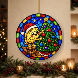 May include: A circular stained glass-style wall hanging featuring a yellow, round character wearing a red and white Santa hat, standing on a small wooden stool to decorate a green Christmas tree with red and blue ornaments and a yellow star.