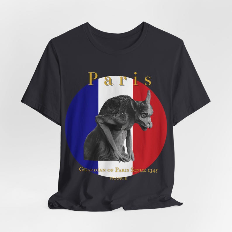 May include: Black t-shirt with a graphic of a gargoyle statue set against a French flag design. The word "Paris" is above the image, with "Guardian of Paris Since 1345 France" below. The design is centered on the shirt.