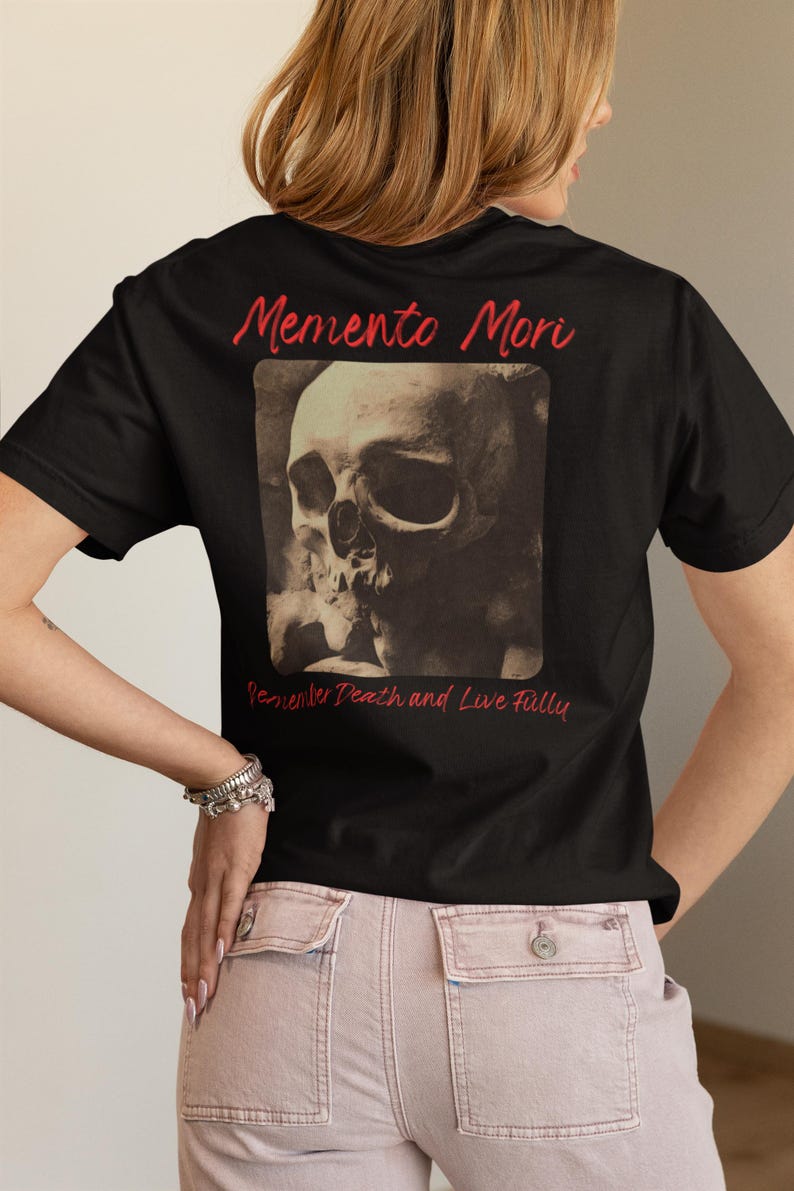 May include: Black t-shirt with a skull graphic and the words "Memento Mori" in red script. The phrase "Remember Death and Live Fully" is below the skull image. The shirt is a classic crew neck.