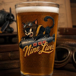 Op de afbeelding: Een helder bierglas gevuld met goudkleurig bier met een afbeelding van een zwarte kat met een vliegeniersbril die op een bom rijdt. De illustratie bevat drie rood-witte zonnesymbolen en de gele cursieve tekst Nine Lives.