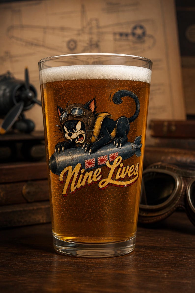 Op de afbeelding: Een helder bierglas gevuld met goudkleurig bier met een afbeelding van een zwarte kat met een vliegeniersbril die op een bom rijdt. De illustratie bevat drie rood-witte zonnesymbolen en de gele cursieve tekst Nine Lives.