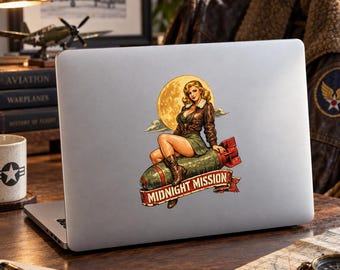 May include: A silver laptop featuring a sticker of a pin-up style illustration. The sticker depicts a person in a brown leather jacket and green skirt sitting on a green bomb against a yellow moon, with a red banner reading MIDNIGHT MISSION.