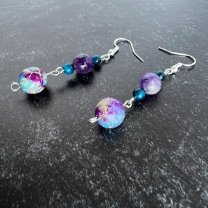 May include: Dangle earrings with a mix of colourful beads. Each earring has a large, round, speckled bead in purple, blue, and pink. The earrings also include a purple amethyst bead and smaller blue beads, all connected with silver-tone metal.